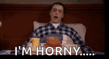 a man in a plaid shirt is laying in bed with a tray of food and the words i 'm horny