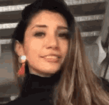 a woman wearing a black turtleneck and red earrings is smiling and looking at the camera .