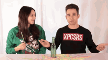 a man wearing a xpcsrs sweater stands next to a woman