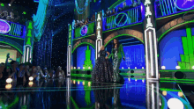 a woman in a green dress stands on a stage in front of a crowd that is watching