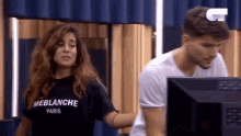 a man and a woman are standing in front of a computer screen .