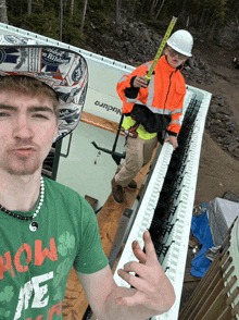 a man wearing a green shirt that says " how me " takes a selfie