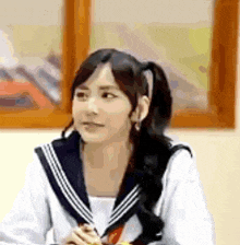 a girl in a sailor suit is sitting in front of a window and looking at something .