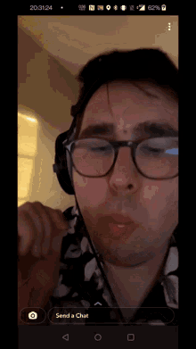 a phone screen shows a man wearing glasses and headphones with a send a chat button