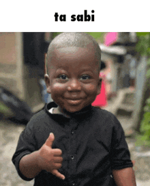 a little boy in a black shirt is giving a thumbs up sign .