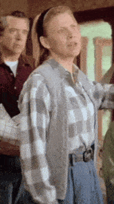 a woman in a plaid shirt and blue pants stands in front of a man