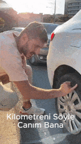 a man is kneeling down next to a white car and pointing to the tire