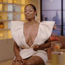 a woman wearing a white dress with a plunging neckline is sitting with her eyes closed