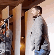 a man is standing in front of a microphone while another man plays a violin behind him .