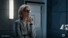 a woman wearing glasses and a suit is sitting in a dark room .