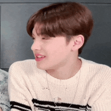 a young man wearing a white sweater and a black and white striped sweater is smiling .