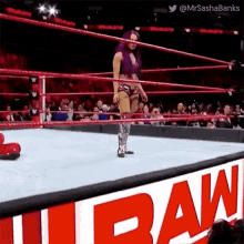 a woman in a purple outfit is standing in a wrestling ring next to a raw sign .