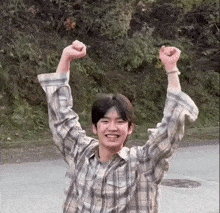 a young man wearing a plaid shirt is raising his arms in the air .