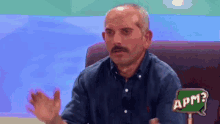 a man with a mustache is sitting in a chair with a sign that says apm .