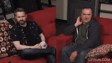 two men are sitting on a red couch with a gifrun.com logo in the corner