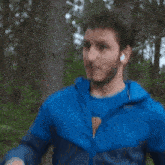 a man wearing ear buds and a blue jacket is running through the woods