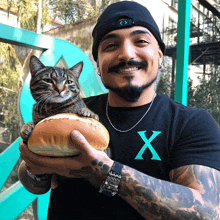 a man is holding a cat on top of a bun and wearing a shirt with the letter x on it