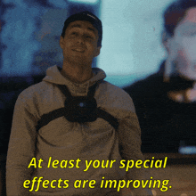 a man wearing a camera on his chest with the words at least your special effects are improving below him