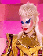 a close up of a drag queen wearing a gold jacket and earrings
