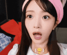 a woman wearing a pink headband and a necklace with a smiley face on it