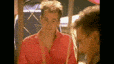 a man in a red shirt is looking at his reflection in a mirror