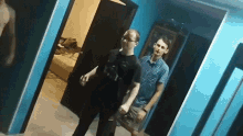 a man in a black shirt is standing next to another man in a blue room .