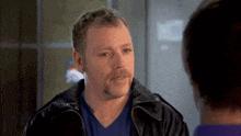 a man with a mustache is wearing a blue shirt and a black leather jacket