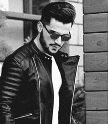 a man wearing sunglasses and a leather jacket is standing next to a wooden wall .
