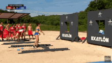 a woman in a bikini is standing in front of a wall that says exatlon