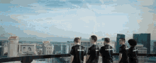 a group of men are standing on a balcony overlooking a city and one of their shirts says bosco