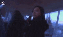 a woman in a black coat is standing in a dark room with a blurred background .