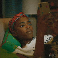 a woman is laying on a couch looking at her cell phone with a netflix logo in the corner