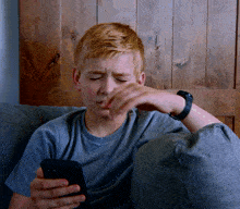 a young boy is sitting on a couch looking at his cell phone