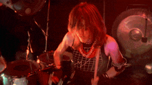 a man in a plaid shirt is playing drums in a dark room