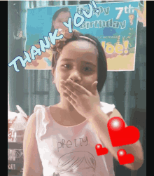 a little girl covering her mouth with her hand in front of a sign that says thank you