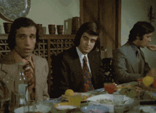 three men are sitting at a table with plates of food and drinks