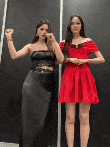 two women standing next to each other one in a red dress and the other in a black dress