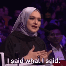 a woman in a hijab is speaking into a microphone and saying `` i said what i said '' .