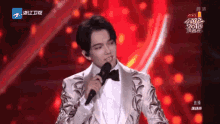 a man in a tuxedo is singing into a microphone on stage .