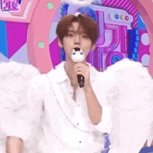 a young man wearing angel wings is holding a microphone .