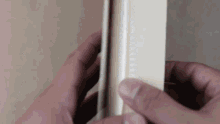 a person is holding a piece of wood in their hands and cutting it .