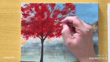 a person is painting a red tree on a canvas
