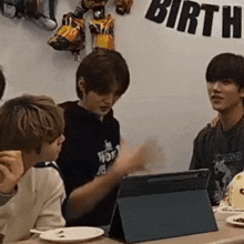 a group of young men are sitting at a table with a tablet and plates of food .
