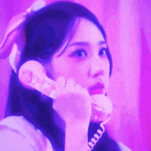 a woman is talking on a pink telephone in front of a pink background .