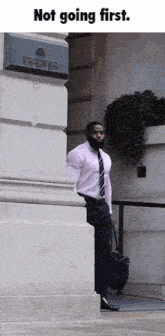 a man in a white shirt and tie is leaning against a wall with the words " not going first " above him
