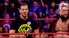 two men are standing in a wrestling ring with a microphone in their hands .