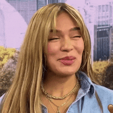 a close up of a woman wearing a necklace and a denim shirt making a funny face .