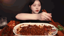 a woman is eating noodles with chopsticks from a plate