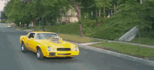 a man in sunglasses is driving a yellow car with a hood scoop