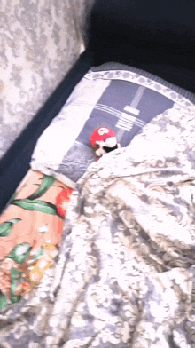 a stuffed mario is laying on a bed with a blanket